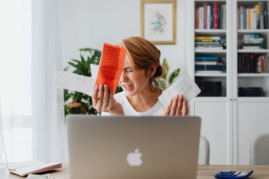 Frustrated woman managing finances, surrounded by bills and a laptop, looking distressed.