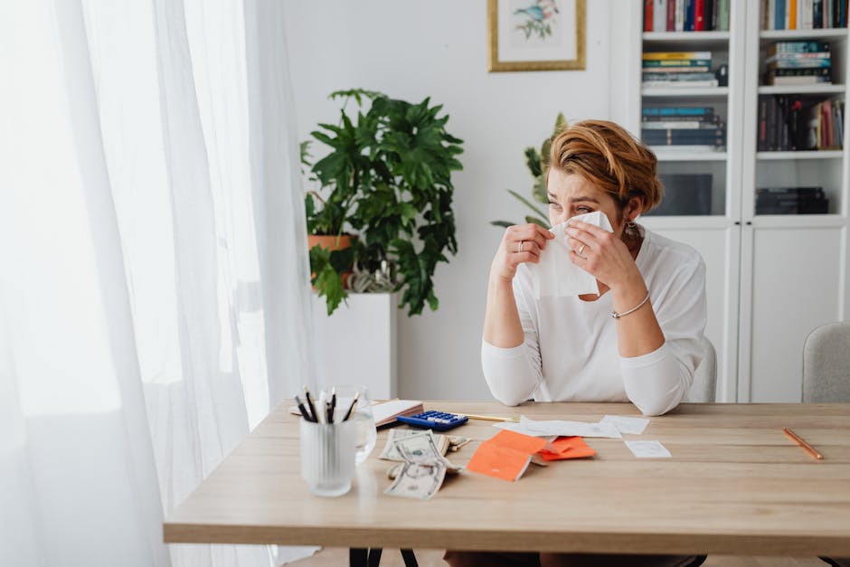 Worried woman at home desk with bills and dollar bills showing financial stress.