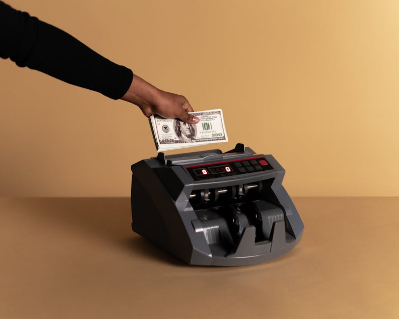 A close-up of a hand using a money counter with US dollar banknotes on a beige background.